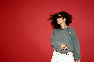 Promotional photo of music artist Lorde on a burgundy background.