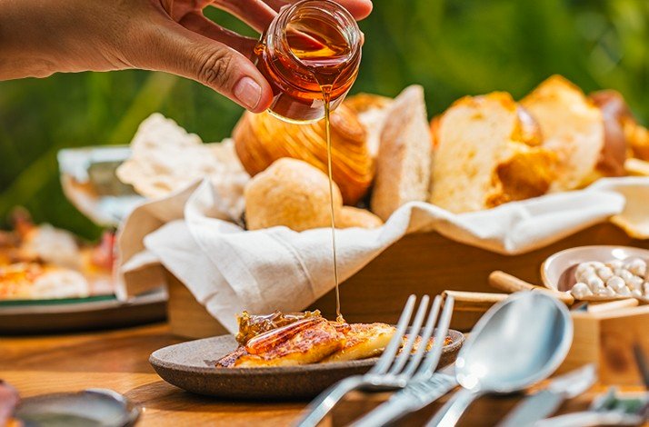 Close-up of a hand pouring honey made by native stingless bees from the Serra da Mantiqueira region over toast at NOTIÊ Restaurante.