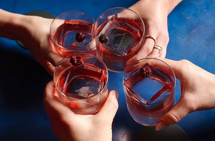 Close up of 4 hands cheering with gin cocktails.