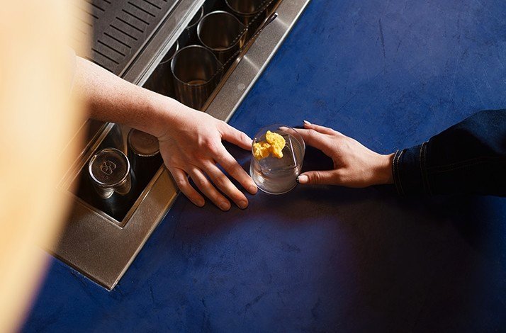 Top-down view at 2 hands holding a gin cocktail on a bar counter.