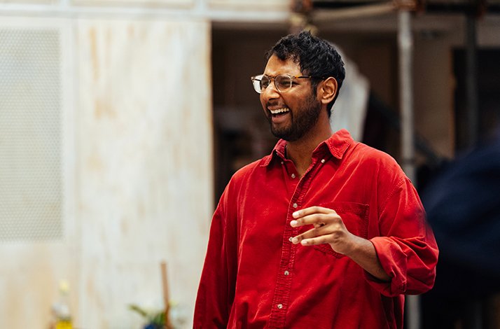 Aaron Gill in a red corduroy shirt, smiling and gesturing expressively during Ilford Boy rehearsals at Donmar Warehouse.