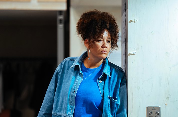  Ebony Molina leaning against a doorframe in rehearsal for Ilford Boy at Donmar Warehouse, wearing a blue denim jacket.