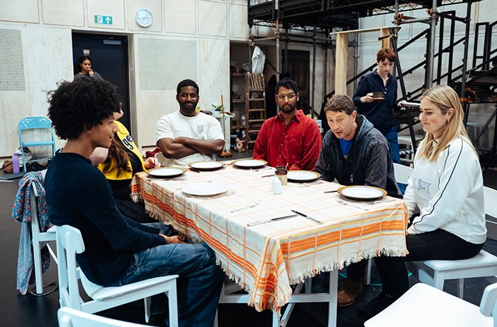 Cast members of Ilford Boy gathered around a laid rehearsal table, engaged in a scene during rehearsals at Donmar Warehouse.
