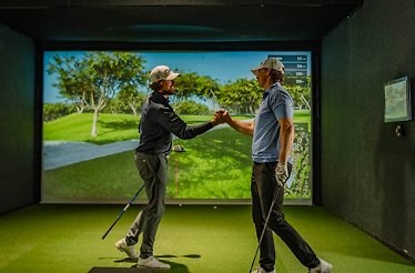 Two golfers shaking hands in an indoor golf simulator.