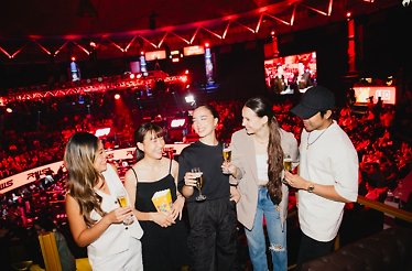 Five young people smiling and enjoying drinks and snacks on a Thai boxing match on the Rajadamnern Stadium in Bangkok Thailand.