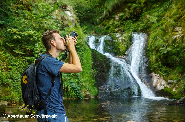 A man taking a photo next to a waterfall. © Abenteur Schwarzbald