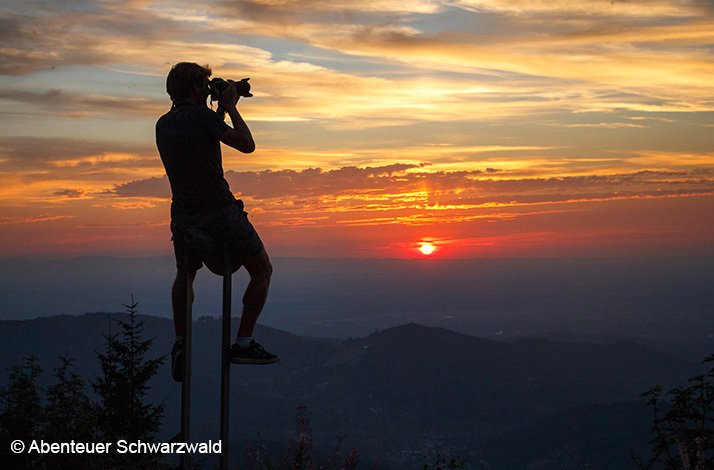 A man at sunset taking a photo while sitting on a high point. © Abenteur Schwarzbald