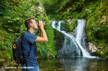 A man taking a photo next to a waterfall. © Abenteur Schwarzbald
