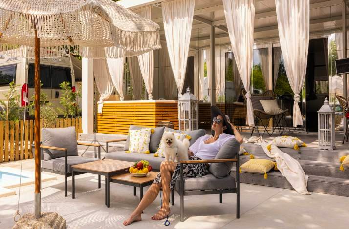 Woman relaxing with a small white dog on an outdoor lounge at a villa terrace at Polidor Camping Resort, Poreč.