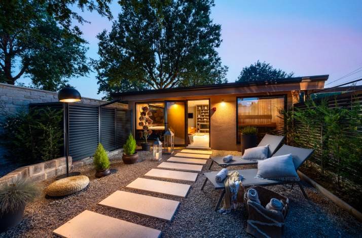 Warmly lit private wellness cabin exterior at dusk, with stepping-stone path and lounge chairs at Polidor Camping Resort.