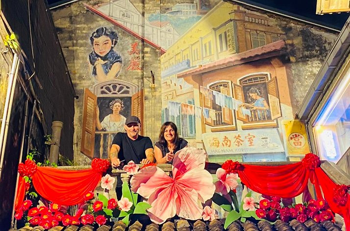 Two participants of guided vespa tour on a balcony of a building with colorful engravings and decorated with flowers.