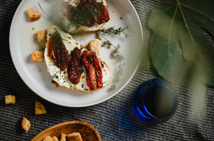 The close shot of a freshly prepared meal - bruschetta with sun dried tomatoes, near the blue glass.