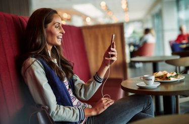 Girl is looking at her phone and laughing in the Costa Coffee cafe with a cup of espresso and sandwiches.