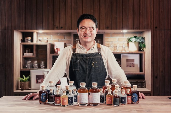 A person smiling presenting various spirits bottles at Compendium Spirits distillery working with barrel aging technology.
