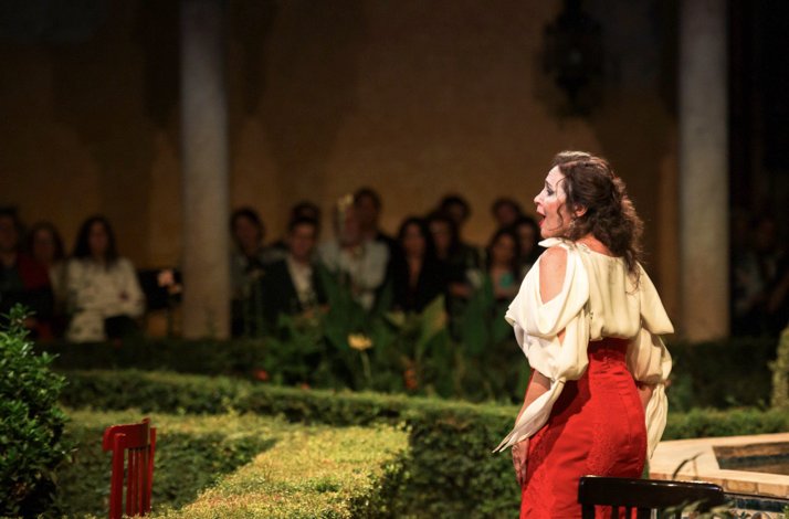 Female Carmen opera performer in red skirt and white blouse performing with back turned, audience watching at Palacio de Las Dueñas.