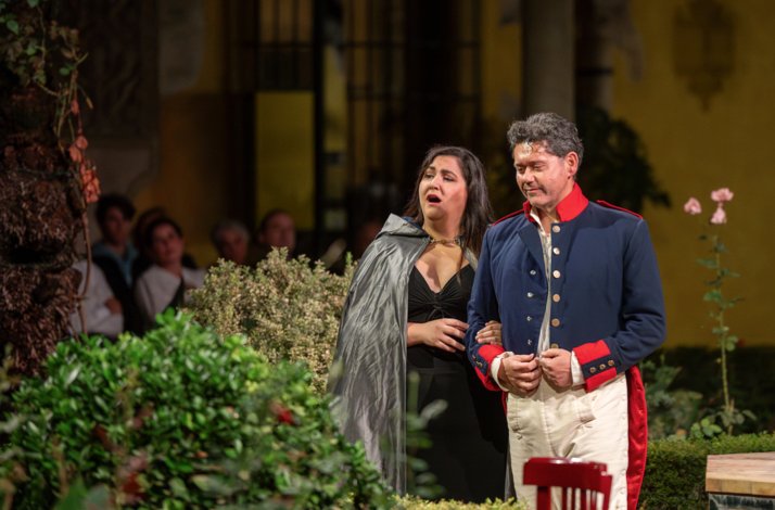 Two Carmen opera performers singing together amid garden greenery at Palacio de Las Dueñas, audience seated in the background.