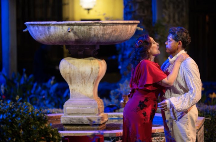 Two Carmen opera performers in an intimate embrace beside a stone fountain at night, Palacio de Las Dueñas, Seville.