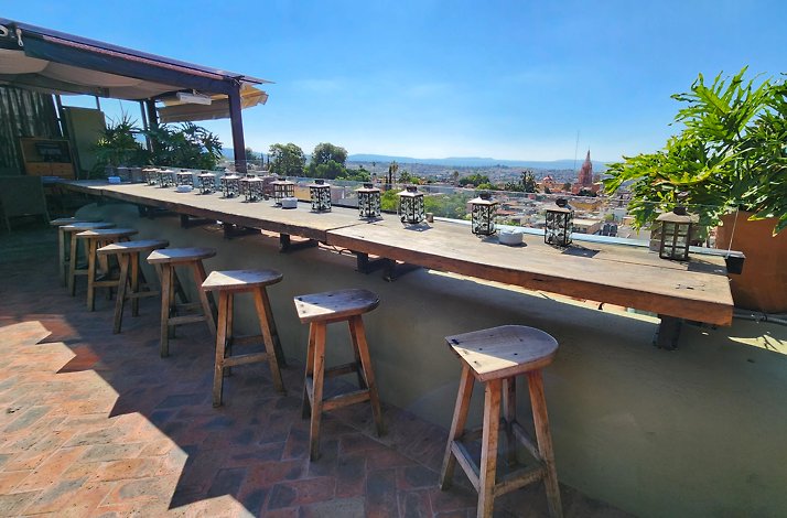 Dining area in the balcony of the Antonia Rooftop Restaurant with wooden bar stools and lamps on the counter.
