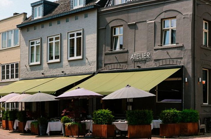 The outdoor terrace of the Atelier restaurant with green awnings, tables, and umbrellas
