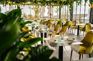 Dinning zone at Veranda dintre Vii with windows and yellow chairs in day time.