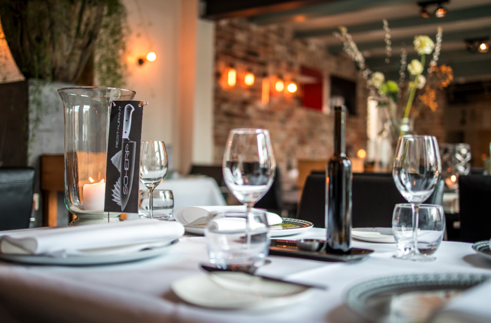 Dining room interior at Restaurant Scherp with white-clothed tables, wine glasses, candlelight, and exposed brick walls.