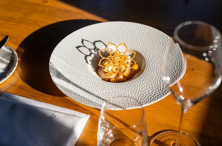 Fine dining dish in a white textured bowl, garnished with a delicate flower-shaped crisp on a wooden table.