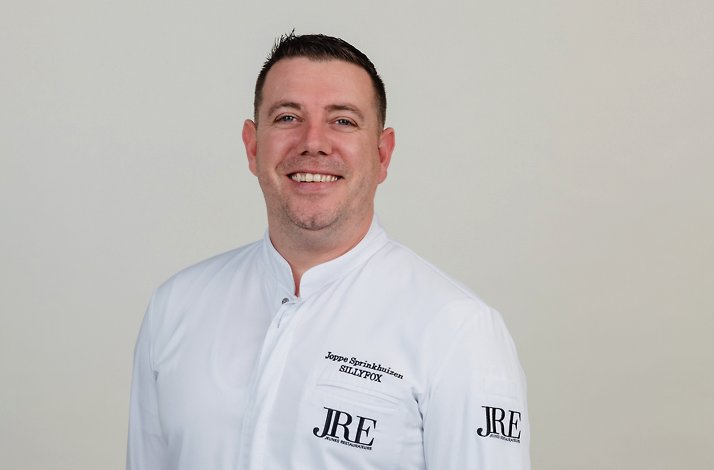 Portrait of a smiling chef in a white SILLYFOX jacket against a light background.