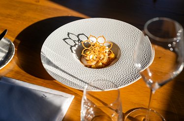 Fine dining dish in a white textured bowl, garnished with a delicate flower-shaped crisp on a wooden table.