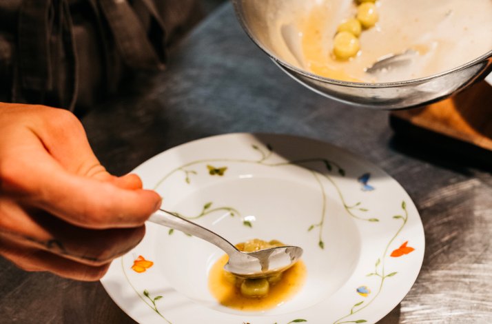 A person is putting a food portion from a cooking saucer into a plate with a spoon.