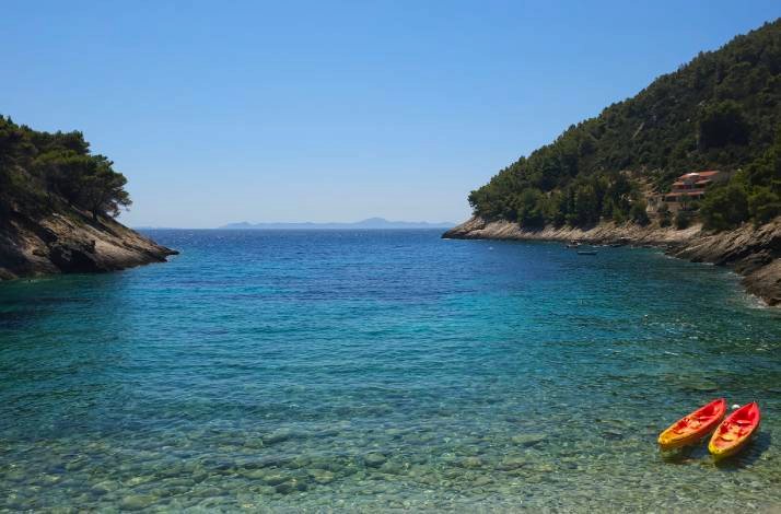 Two colorful kayaks resting on the sandy shore beside a clear blue ocean under a bright sky.