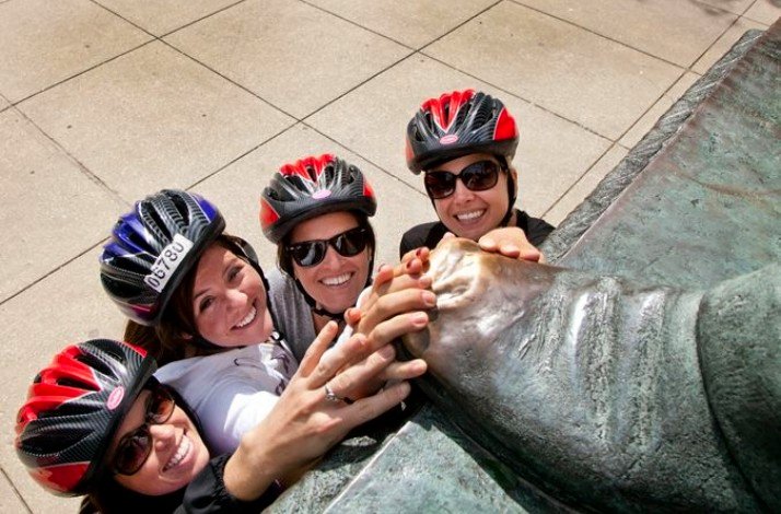 4 participants of the Chicago bike tour touching a foot of a statue for luck.