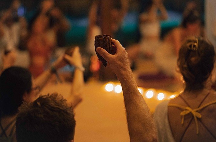 Close focus on a raised hand holding a cocoa fruit during an exclusive private cacao ceremony.