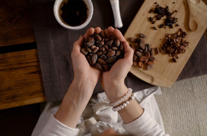 A handful of cocoa seeds captured from above a table with chopping devices and a glass of hot drink.