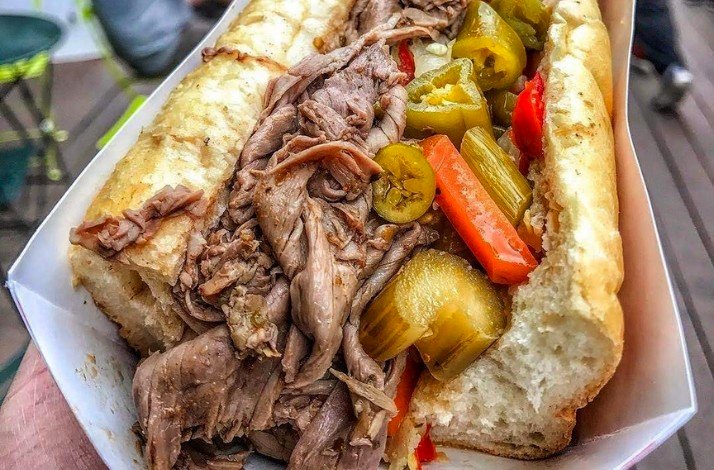 A hotdog filled with chopped meat with pickles and vegetables