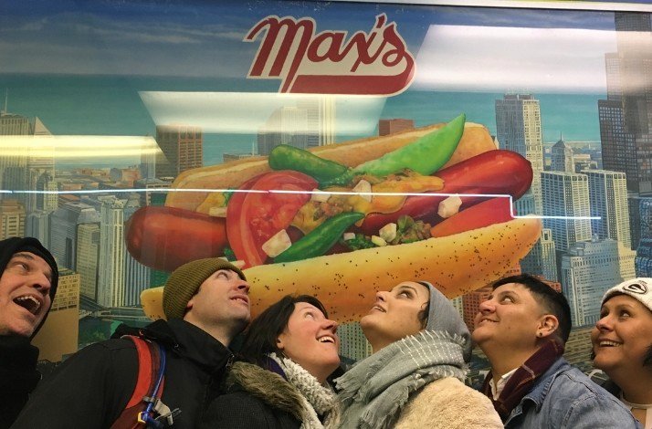 A group of people with a large hotdog advertisement sign behind them