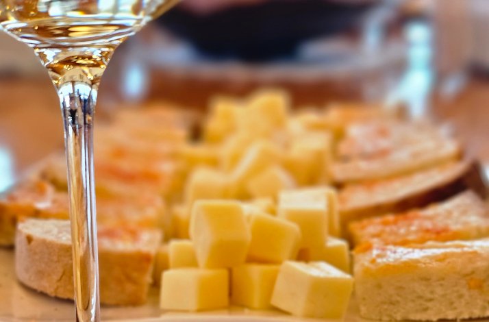 A board with cheeses and breads accompanied by a glass of wine