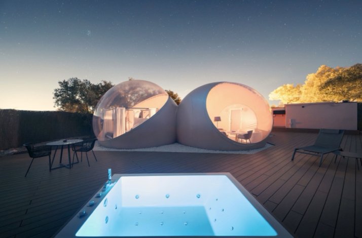 Two interconnected bubble domes at Miluna Open Nature Rooms at twilight, with a lit outdoor jacuzzi and deck in the foreground.