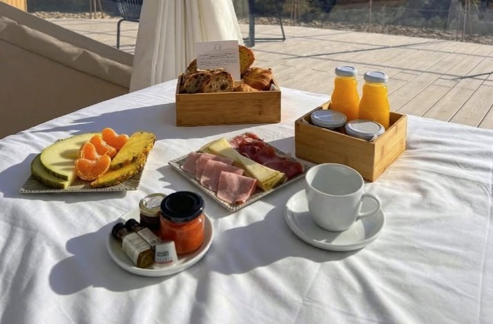 Gourmet breakfast spread on a white-clothed outdoor table, featuring fresh fruit, charcuterie, pastries, juices, and coffee.
