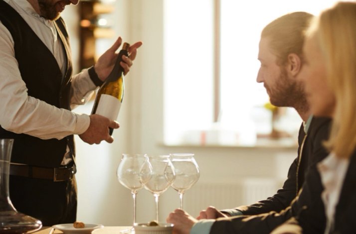 Couple seated at a table being served white wine by a sommelier during an intimate private tasting session.