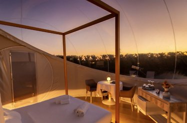 Interior of Miluna's 'Lunas de Urano' bubble suite at sunset, with a canopy bed, dining table, and telescope amid nature views.