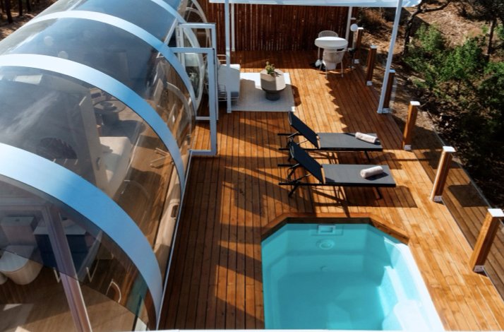 Aerial view of a Crystal Suite's curved glass structure beside a private pool and wooden sun deck at La Dehesa Experiences.