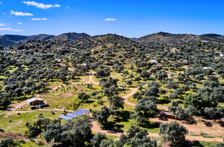 Aerial panorama of La Dehesa Experiences' protected Sierra Morena landscape, dotted with holm oaks, solar panels, and guest suites.
