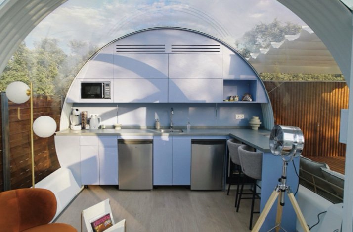 Interior of a Crystal Suite at La Dehesa Experiences, featuring a curved glass ceiling, kitchenette, and bar seating.