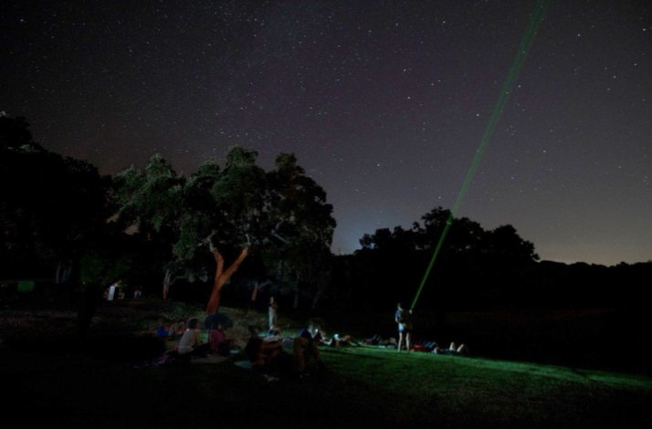  Group of guests lying on grass beneath a dark, star-scattered sky as a guide traces constellations with a laser pointer.