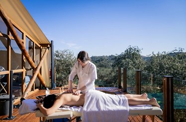 Guest receiving a back massage on an open-air deck at La Dehesa Experiences, with woodland scenery beyond.