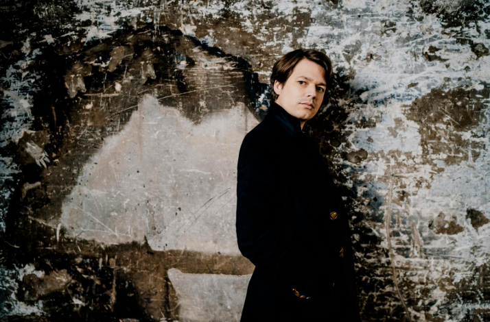 David Fray posing in a black coat near a gray and black wall.