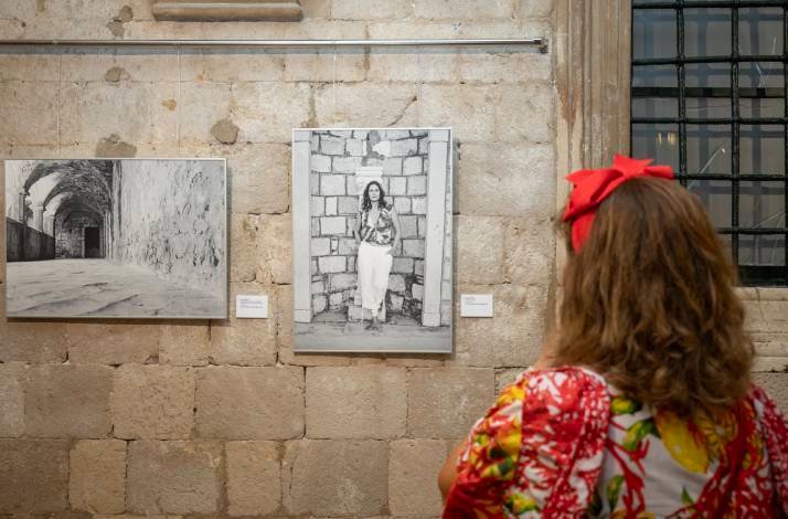 A woman in a red bow observing black-and-white photos displayed on a stone wall.