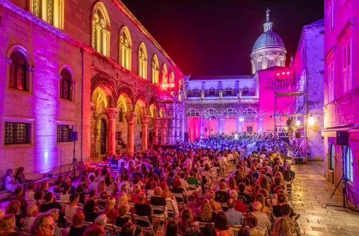 An open-air classical concert at night in Dubrovnik Summer Festival, with historic buildings illuminated in bright pink light.