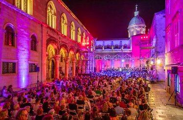 An open-air classical concert at night in Dubrovnik Summer Festival, with historic buildings illuminated in bright pink light.