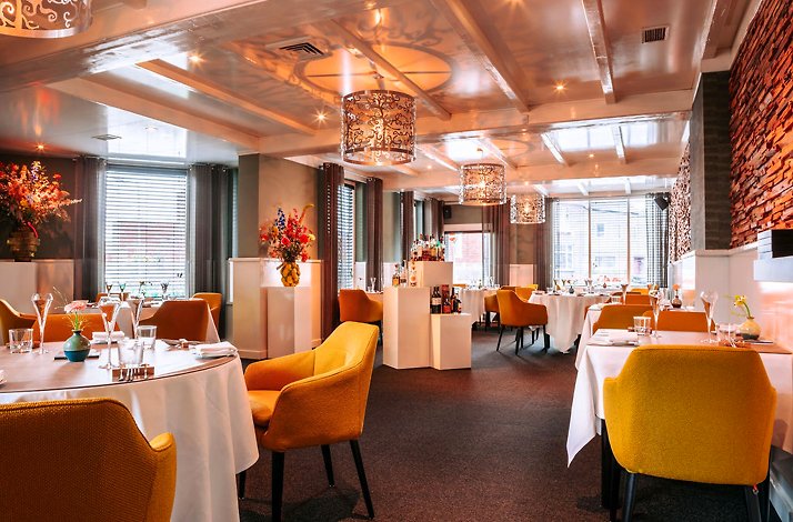 Dining room interior at De Beejekurf with white tablecloths, warm lighting and modern chairs.